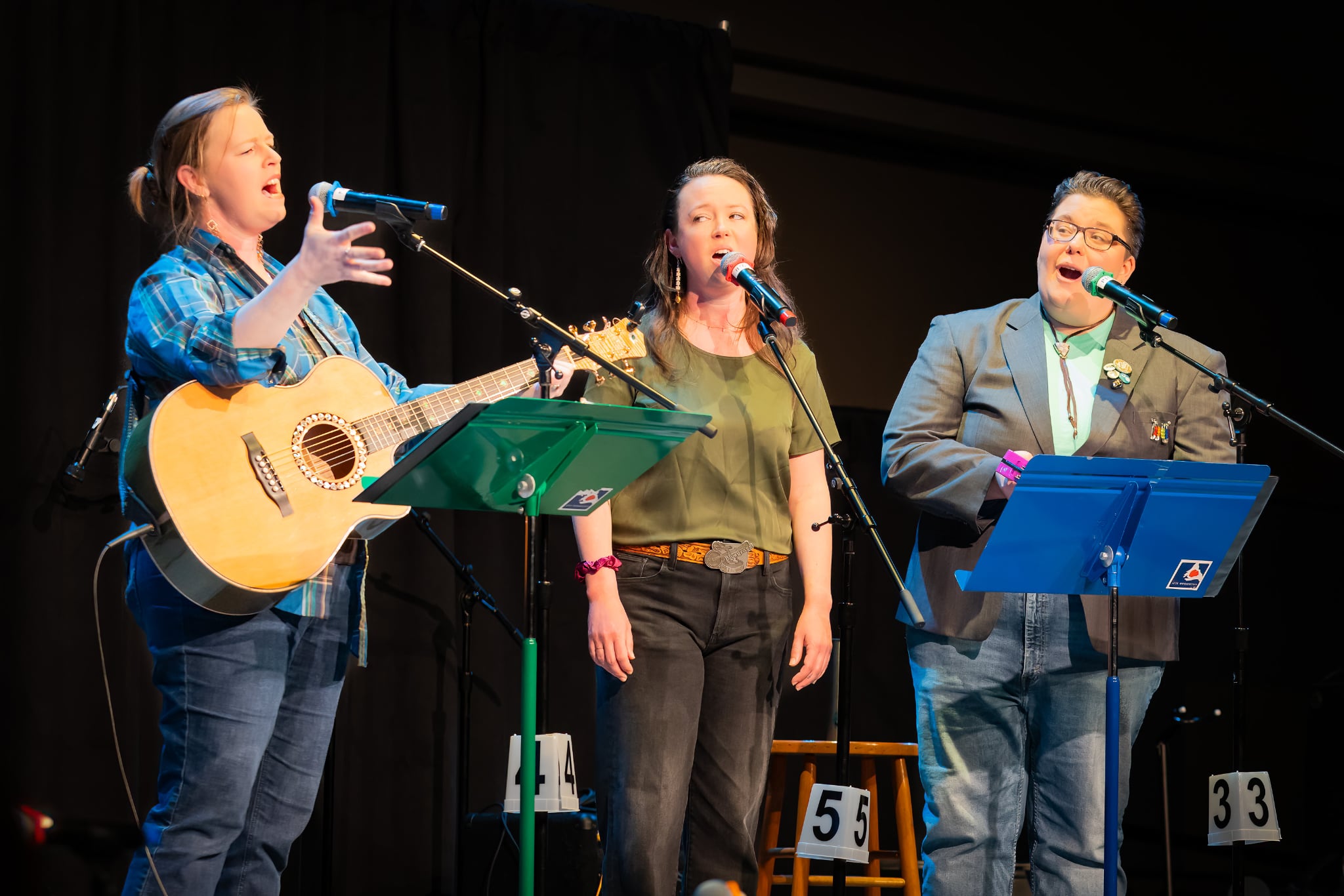 Photograph of Marian Call, Cate Ross, and Kelsey Riker performing on the Alaska Folk Festival stage in 2026. Photo by Brian Wallace.